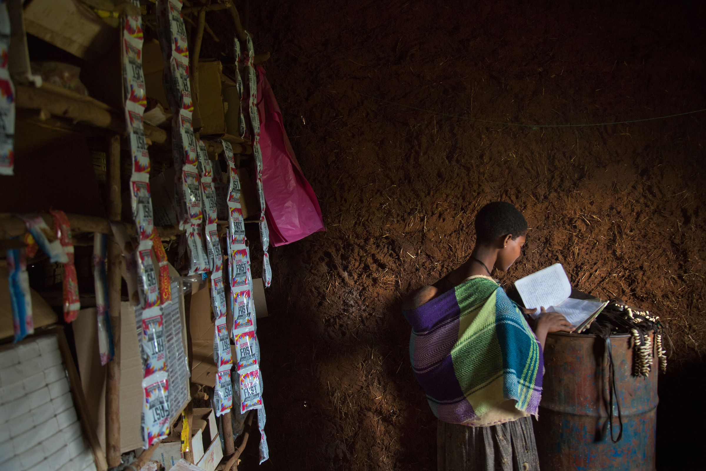 Destaye, 15, looks through her old schoolbooks in the store she and her husband Addisu, 27, run out of their home.